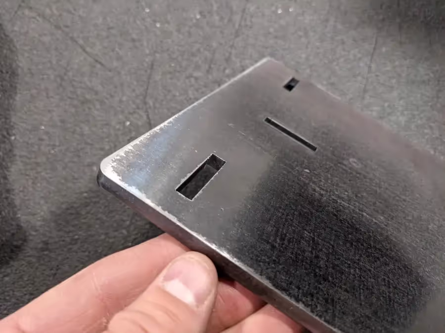 A hand holds a laser cut and deburred piece of steel at an angle